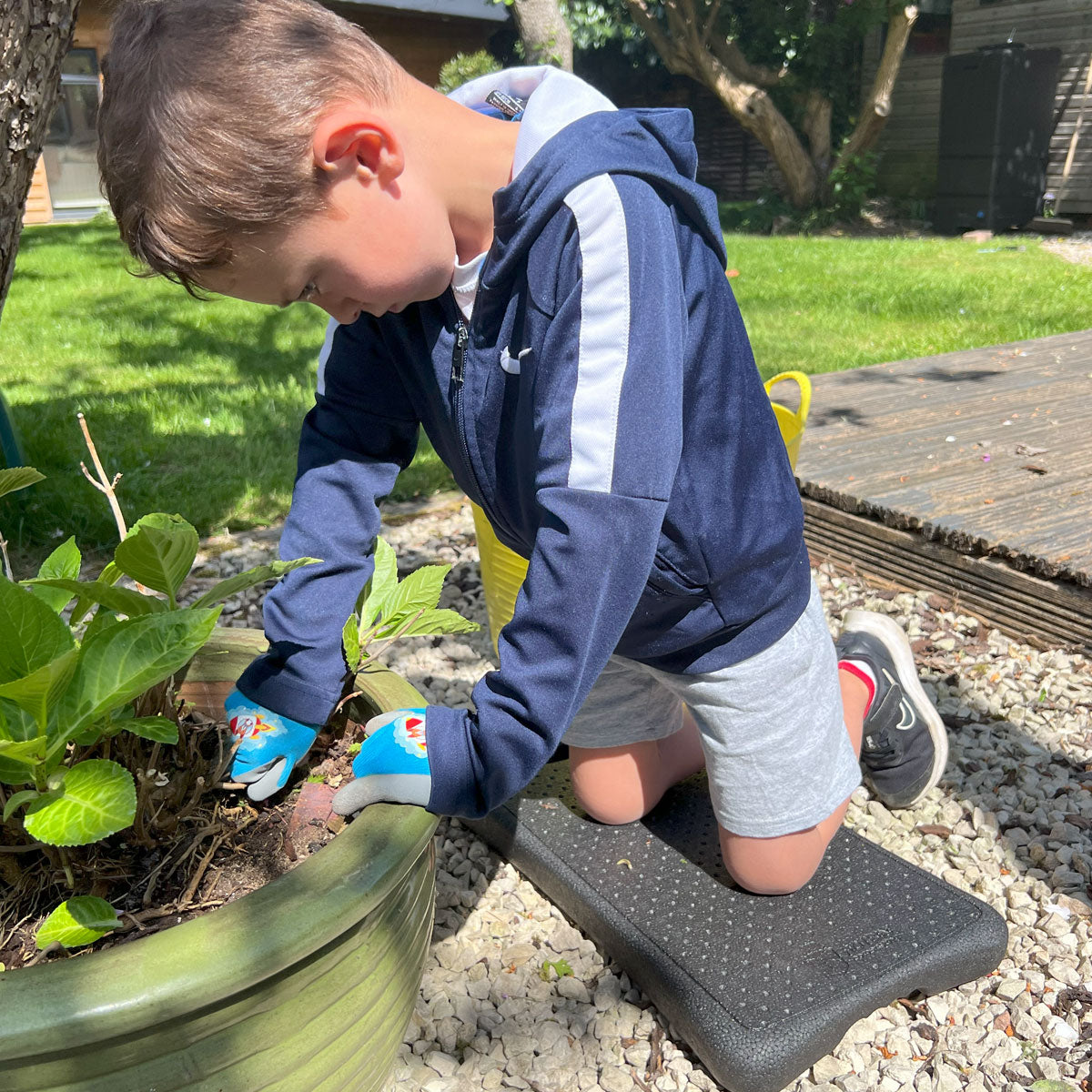 Child weeding using a Genden kneeler outdoors on a gravel surface.
